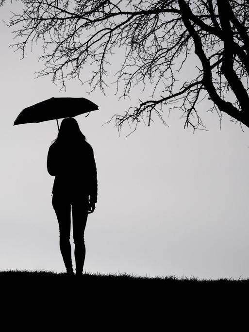 Eine Frau steht bei trübem Wetter unter einem kahlen Baum, die Aufnahme ist in schwarz-weiß.