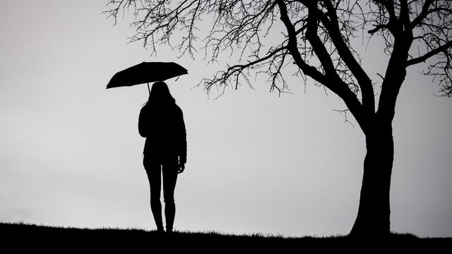 Eine Frau steht bei trübem Wetter unter einem kahlen Baum, die Aufnahme ist in schwarz-weiß.