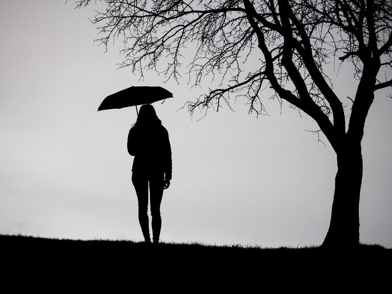 Eine Frau steht bei trübem Wetter unter einem kahlen Baum, die Aufnahme ist in schwarz-weiß.