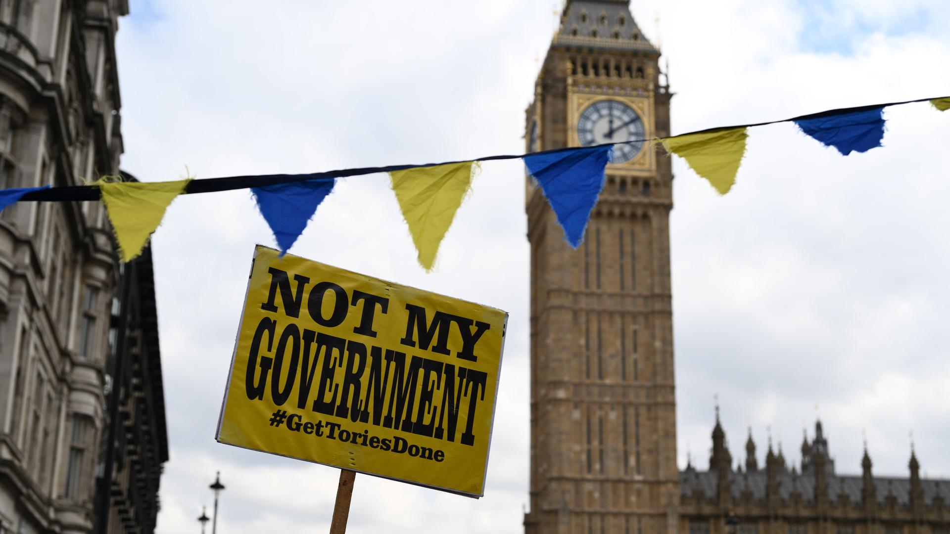 Ein Schild mit der Aufschrift "Not my government, get tories done" wird bei einer Demonstration am Londoner Big Ben hochgehalten.