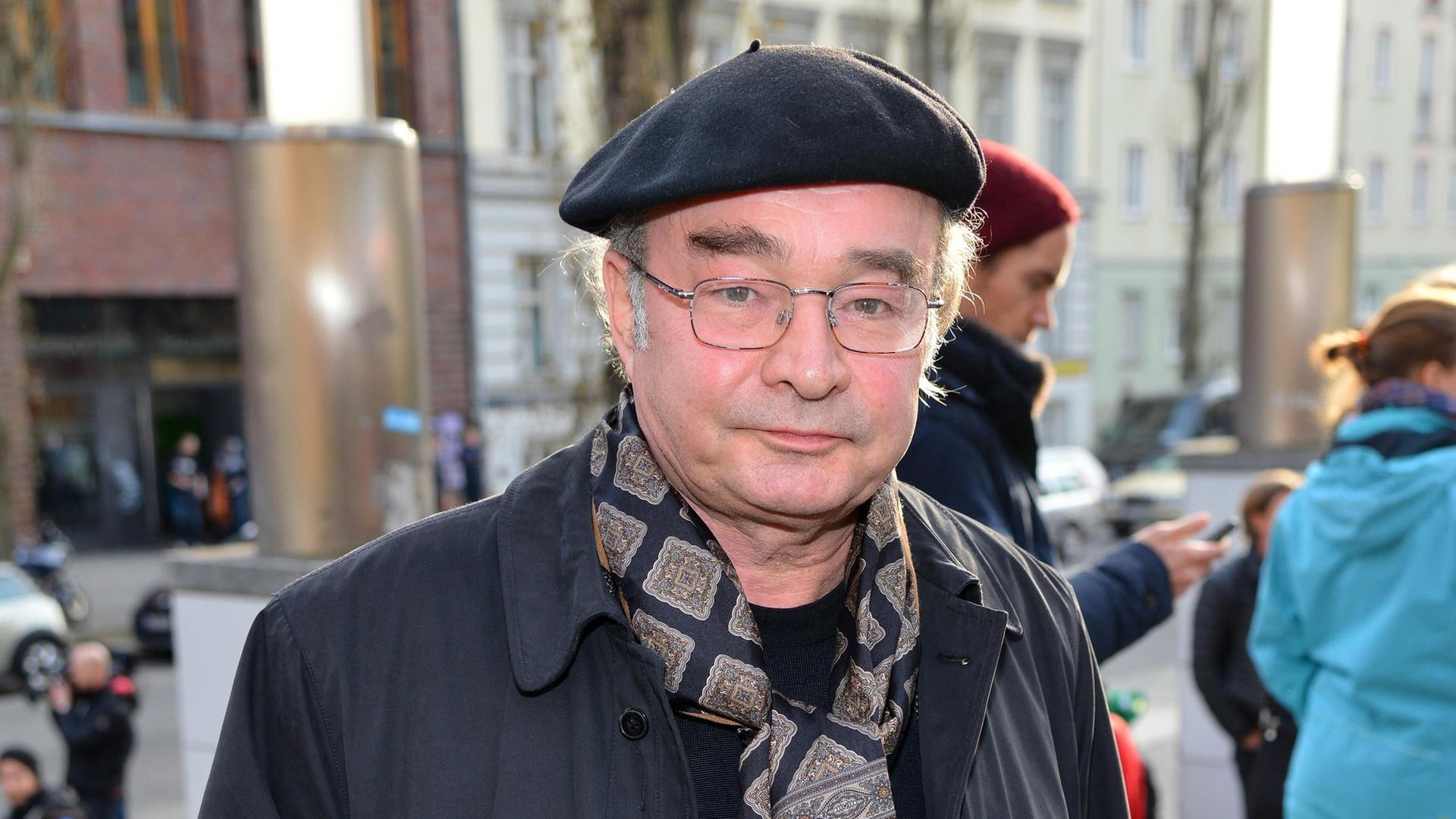 Martin Seifert schaut in die Kamera. Er trägt eine schwarze Baskenmütze und einen Schal mit braunem Paisleymuster.