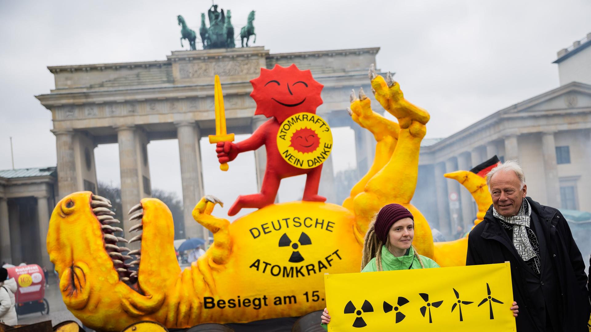 Jürgen Trittin (Bündnis 90/Die Grünen), Mitglied des Deutschen Bundestages und ehemaliger Umweltminister, steht neben einer Aktivistin vor einer Dinosaurier-Figur und der roten Sonne, teil des Anti-Atomkraft-Logos, bei einer Aktion der Umweltorganisation Greenpeace vor dem Brandenburger Tor.