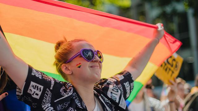 Eine Frau mit Regenbogen-Fahne nimmt an einer Parade zum "Christopher Street Day" teil.