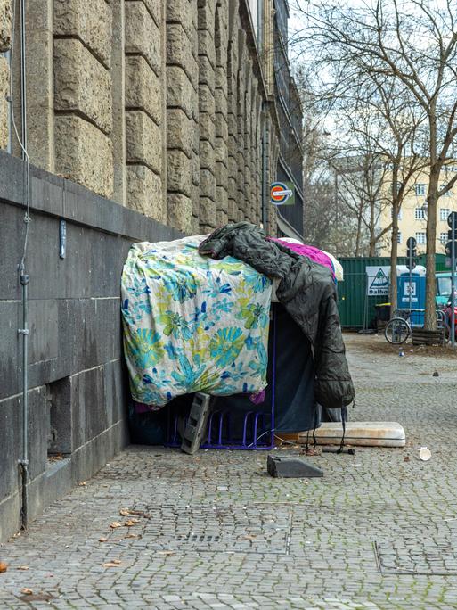 Provisorisch aufgetürmte, schmutzige Bettdecken und Schlafsäcke, die als Unterschlupf für einen Obdachlosen an der Ecke der Ganghoferstraße dienen