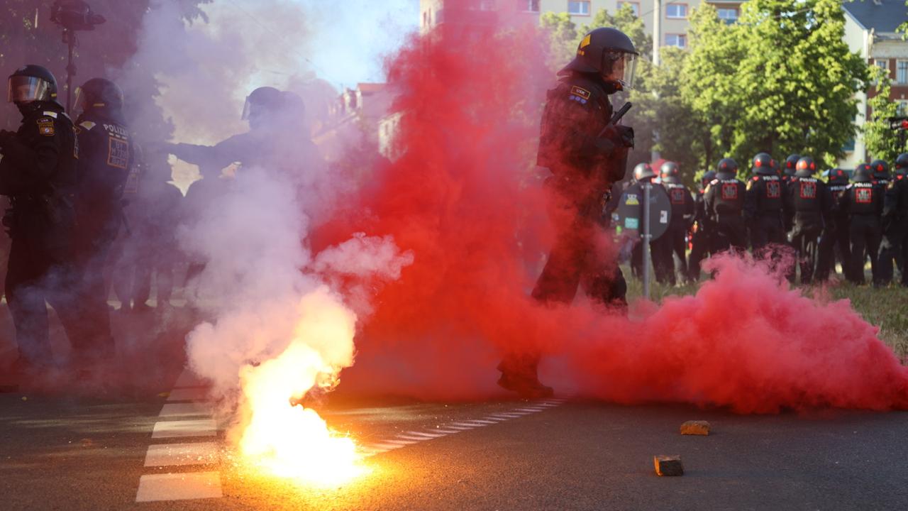In Leipzig laufen Polizisten über eine Straße, auf der Pyrotechnik abbrennt, eine rote Rauchwolke ist zu sehen.