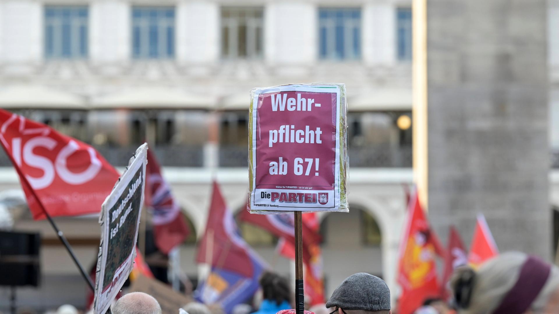 Bei einer Demonstration wird ein Schild von der Partei "Die PARTEI" in die Höhe gehalten. Darauf steht: "Wehrpflicht mit 67!"