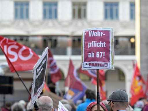 Bei einer Demonstration wird ein Schild von der Partei "Die PARTEI" in die Höhe gehalten. Darauf steht: "Wehrpflicht mit 67!"