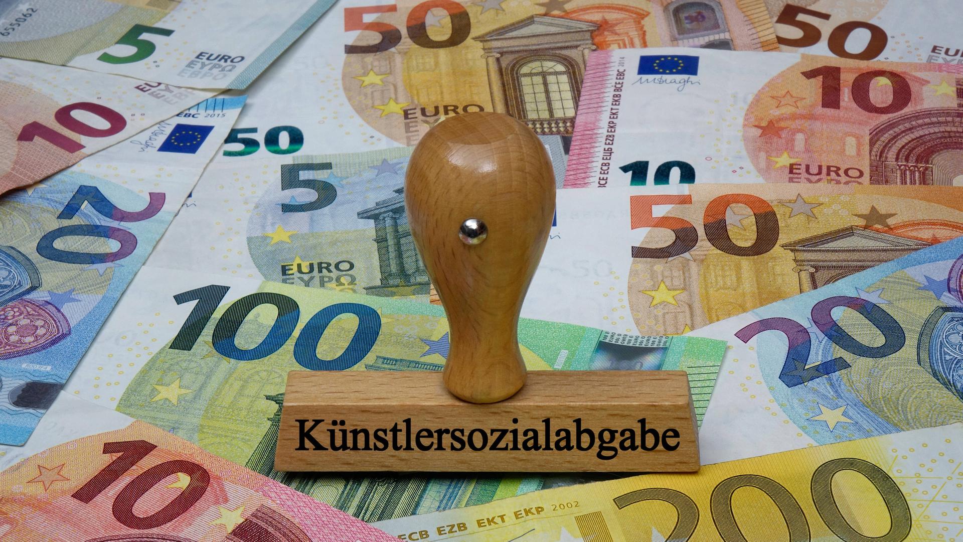 Ein Stempel mit der Aufschrift "Künstlersozialabgabe" steht auf Banknoten.