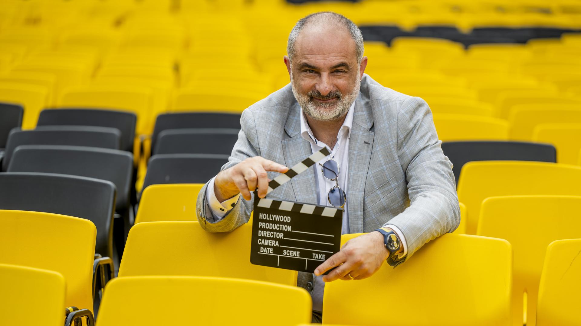 Der künstlerische Leiter des Filmfestivals in Locarno, Giona A. Nazzaro, inmitten von gelben Stühlen mit einer Filmklappe in der Hand. 