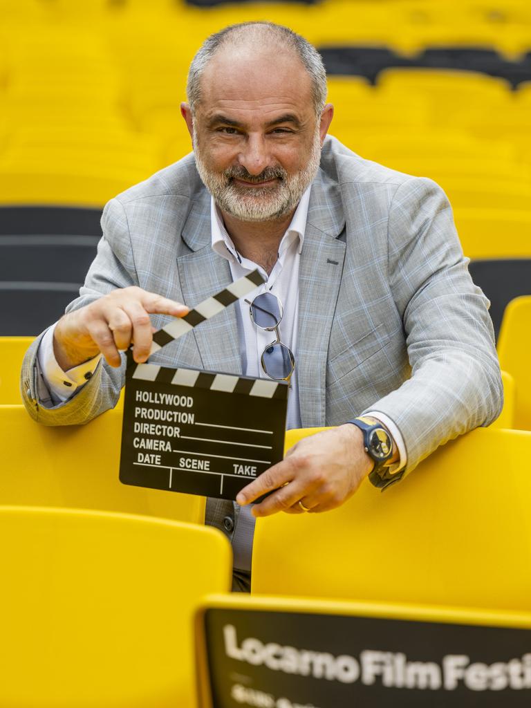 Der künstlerische Leiter des Filmfestivals in Locarno, Giona A. Nazzaro, inmitten von gelben Stühlen mit einer Filmklappe in der Hand. 