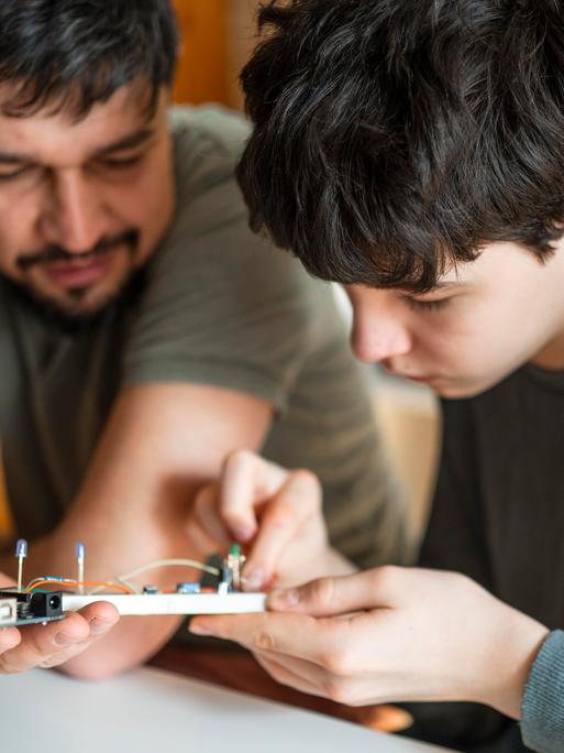 Ein Vater hilft seinem Sohn bei der Reparatur eines elektronischem Geräts