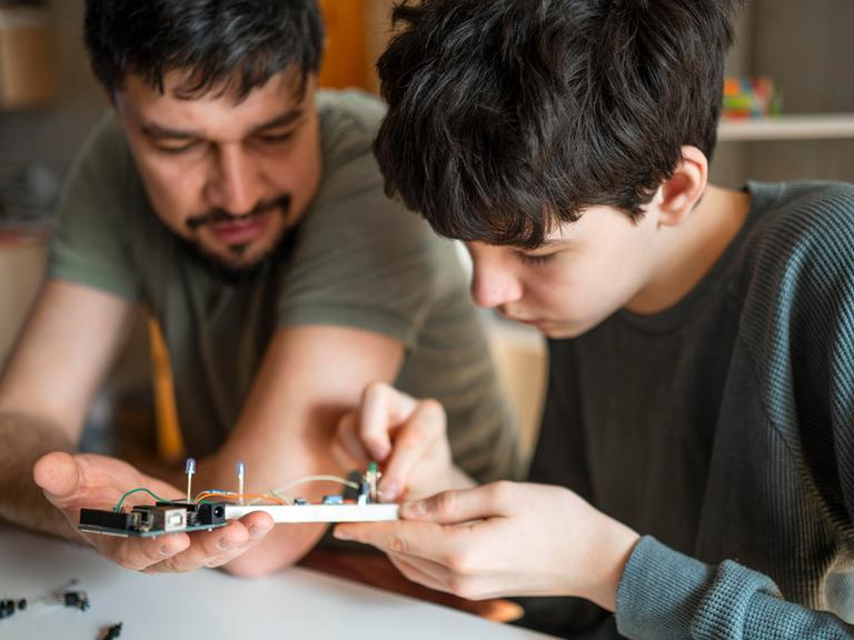 Ein Vater hilft seinem Sohn bei der Reparatur eines elektronischem Geräts