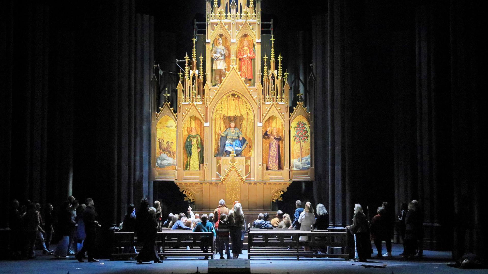 Blick auf einen Hochaltar, der viele goldene Passagen zeigt. Menschen bestaunen den Altar. 