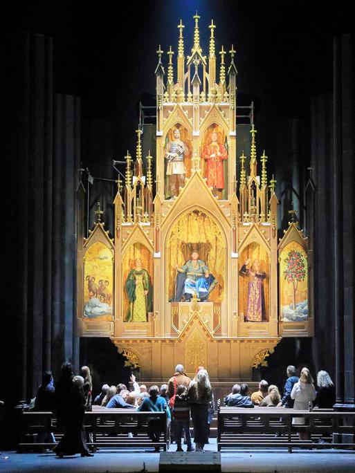 Blick auf einen Hochaltar, der viele goldene Passagen zeigt. Menschen bestaunen den Altar. 