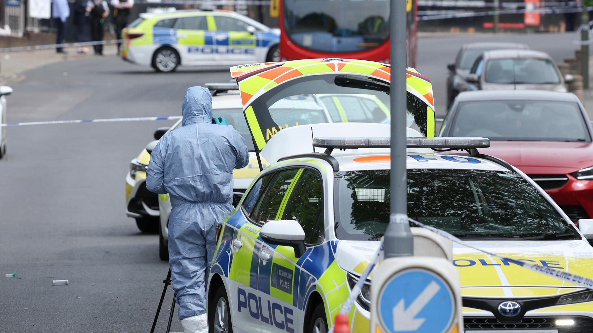 Kriminaltechniker der Polizei am Tatort in London. Mehrere Polizeiautos und ein Absperrband sind zu sehen.