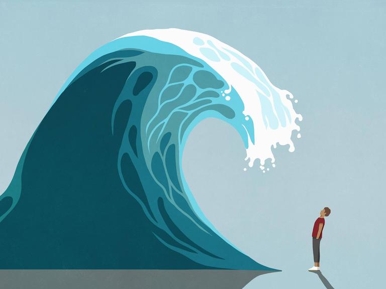 Ein Mensch steht vor einer Welle, welche ihn um ein vielfaches überragt.
