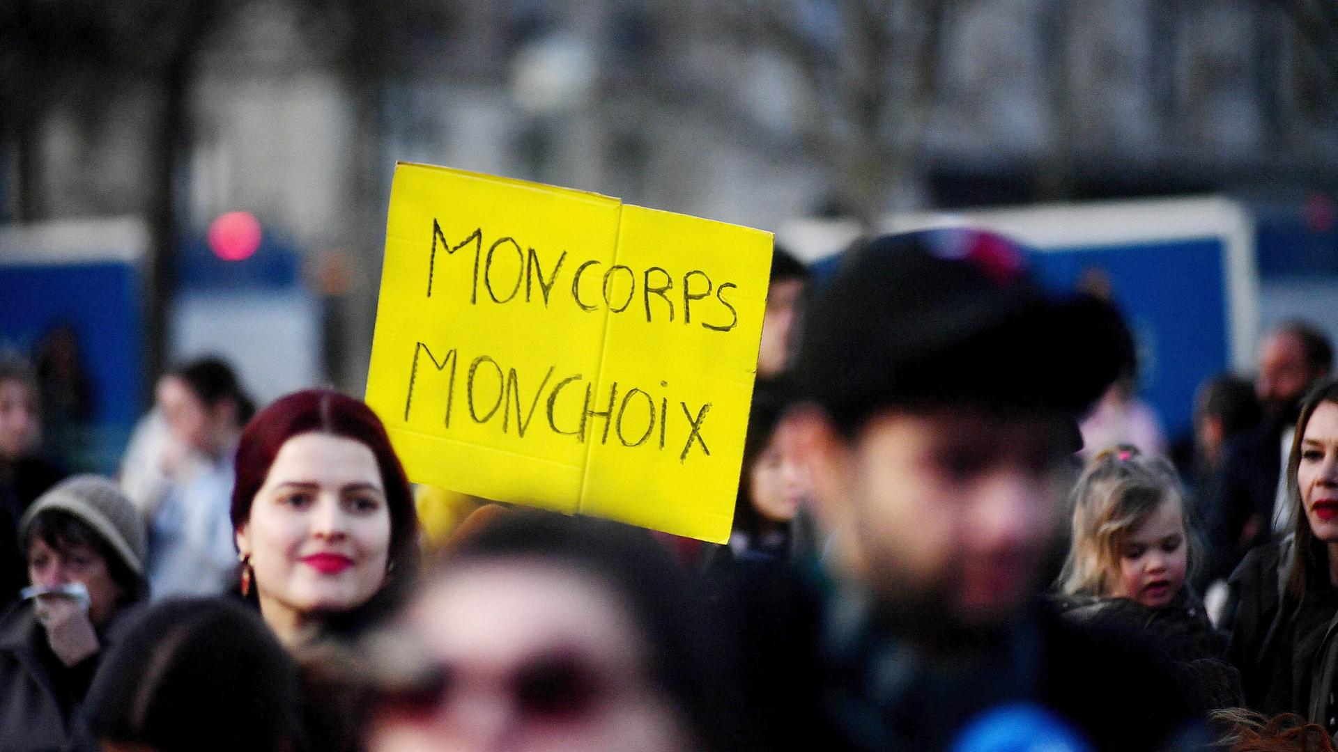 Menschen versammeln sich in der Nähe des Eiffelturms auf dem Place du Trocadero in Paris, Frankreich, am 4. März 2024. Eine Frau trägt ein gelbes Plakat mit den Worten "MON CORPS MON CHOIX".