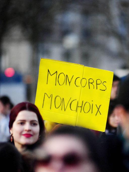 Menschen versammeln sich in der Nähe des Eiffelturms auf dem Place du Trocadero in Paris, Frankreich, am 4. März 2024. Eine Frau trägt ein gelbes Plakat mit den Worten "MON CORPS MON CHOIX".