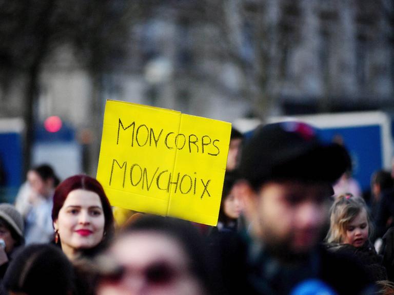 Menschen versammeln sich in der Nähe des Eiffelturms auf dem Place du Trocadero in Paris, Frankreich, am 4. März 2024. Eine Frau trägt ein gelbes Plakat mit den Worten "MON CORPS MON CHOIX".