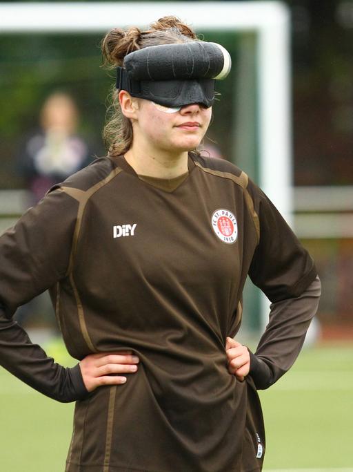 Blindenfußballerin Thoya Küster während eines Spiels für den FC St. Pauli mit Sichtschutz vor den Augen. Ihre Hände hat sie in die Hüften gestemmt.