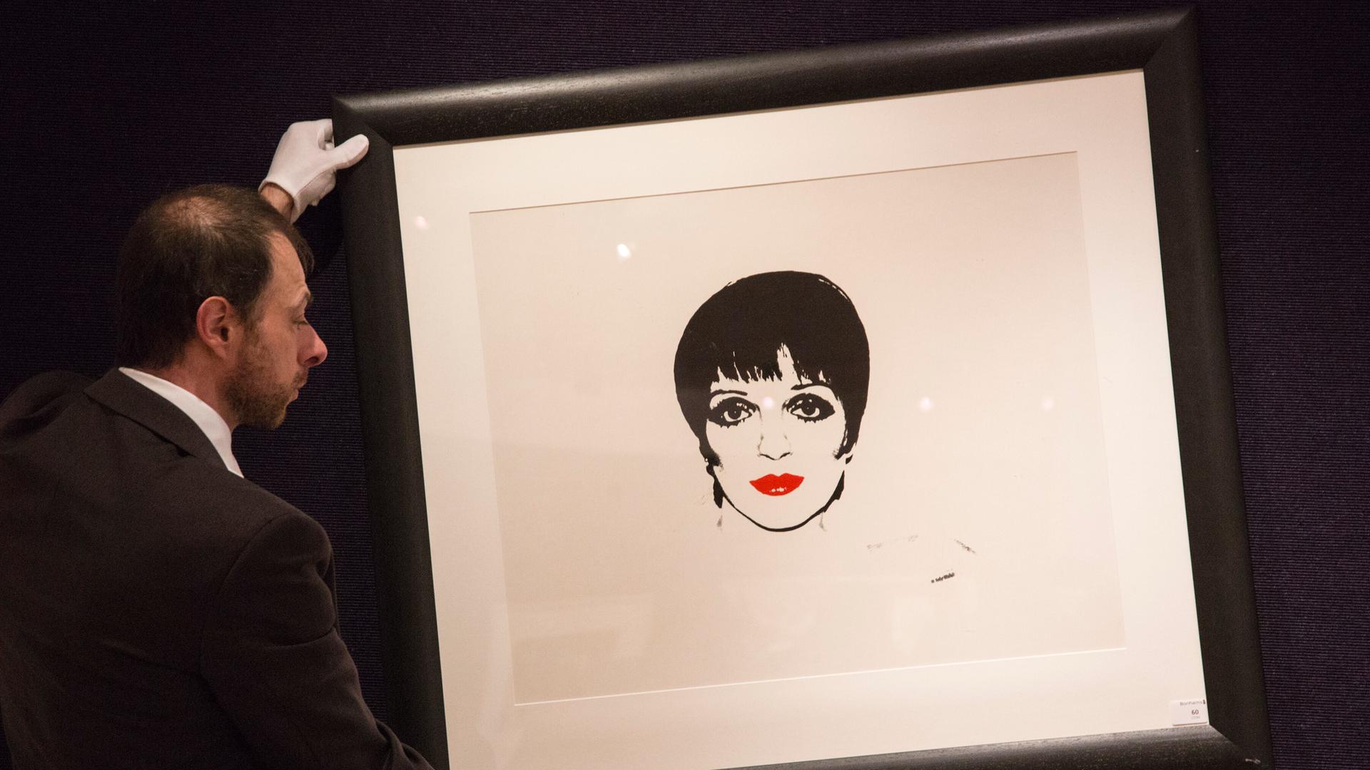 Ein Mann mit weißen Handschuhen hält ein Bild der Schauspielerin Liza Minelli von Andy Warhol. Ein Mann mit weißen Handschuhen hält ein Bild der Schauspielerin Liza Minelli von Andy Warhol.