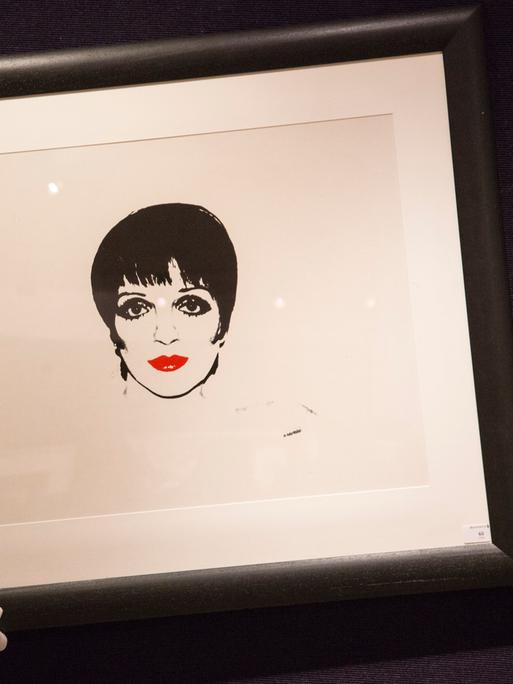 Ein Mann mit weißen Handschuhen hält ein Bild der Schauspielerin Liza Minelli von Andy Warhol.