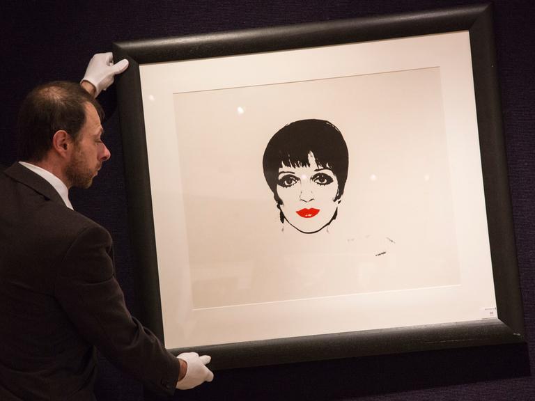 Ein Mann mit weißen Handschuhen hält ein Bild der Schauspielerin Liza Minelli von Andy Warhol.