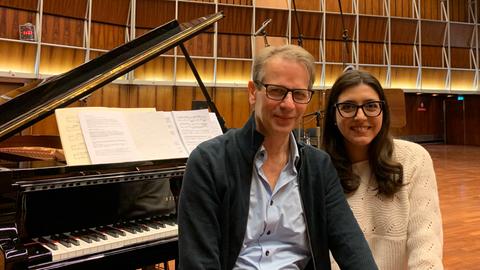 Christoph Schmitz sitzt neben Sophie Pacini auf einer Klavierbank vor dem aufgeklappten Flügel im Kammermusiksaal Köln.