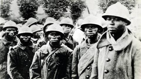 Eine Gruppe Soldaten afrikanischer Abstammung stehen mit militärischer Kleidung eng beieinander und schauten besorgt in die Kamera.