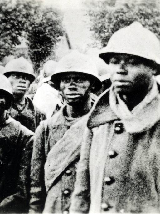 Eine Gruppe Soldaten afrikanischer Abstammung stehen mit militärischer Kleidung eng beieinander und schauten besorgt in die Kamera.