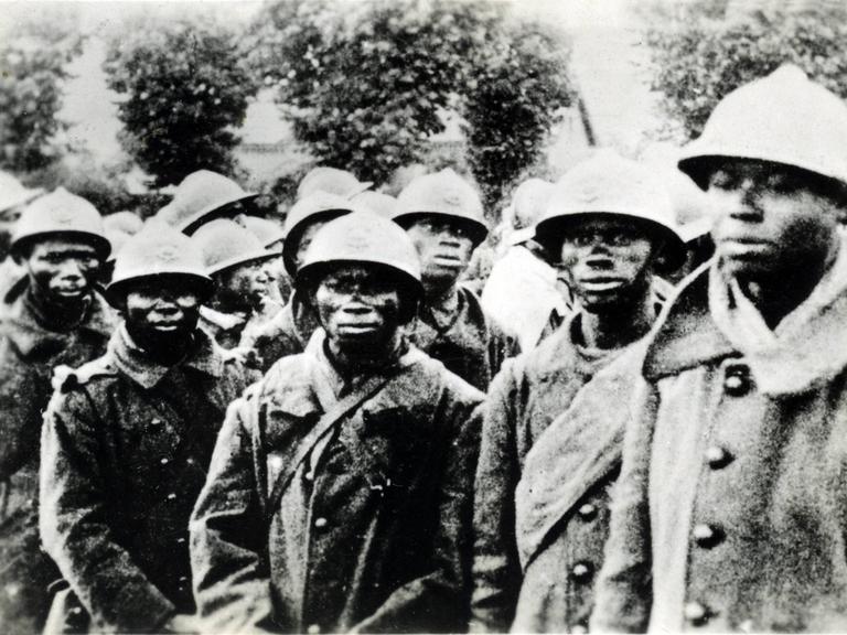 Eine Gruppe Soldaten afrikanischer Abstammung stehen mit militärischer Kleidung eng beieinander und schauten besorgt in die Kamera.