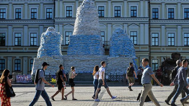 Ein mit Sandsäcken verhülltes Monument in Borodyanka, Ukraine. Davor gehen Leute vorbei.