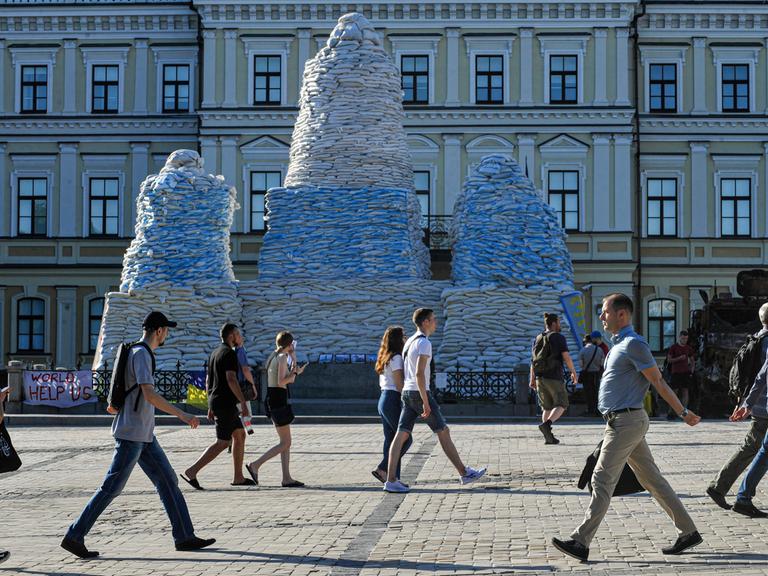 Ein mit Sandsäcken verhülltes Monument in Borodyanka, Ukraine. Davor gehen Leute vorbei.