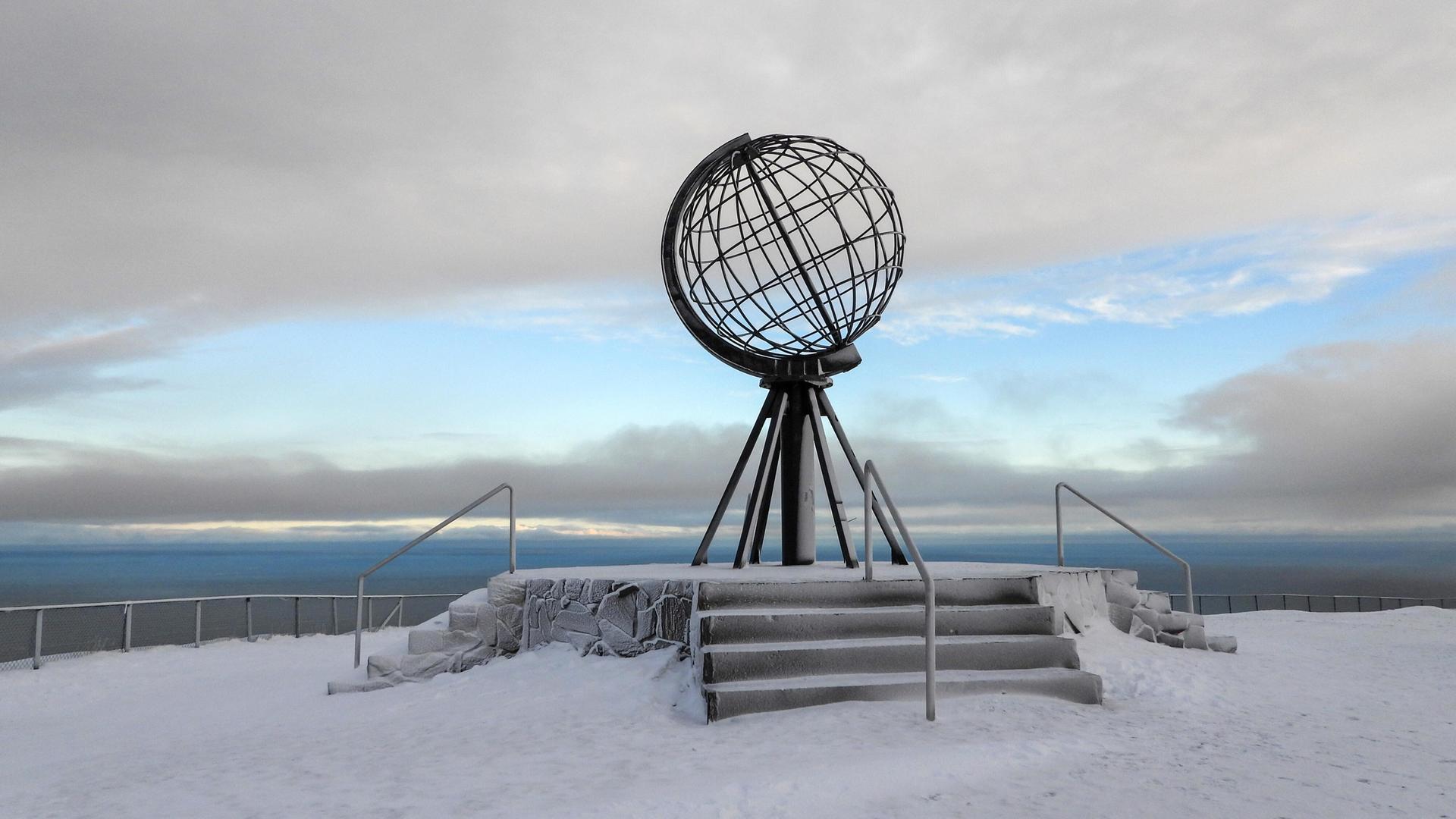 Eine Globus Skulptur der Erdkugel steht am Nordkap in Norwegen auf Schnee und Eis.