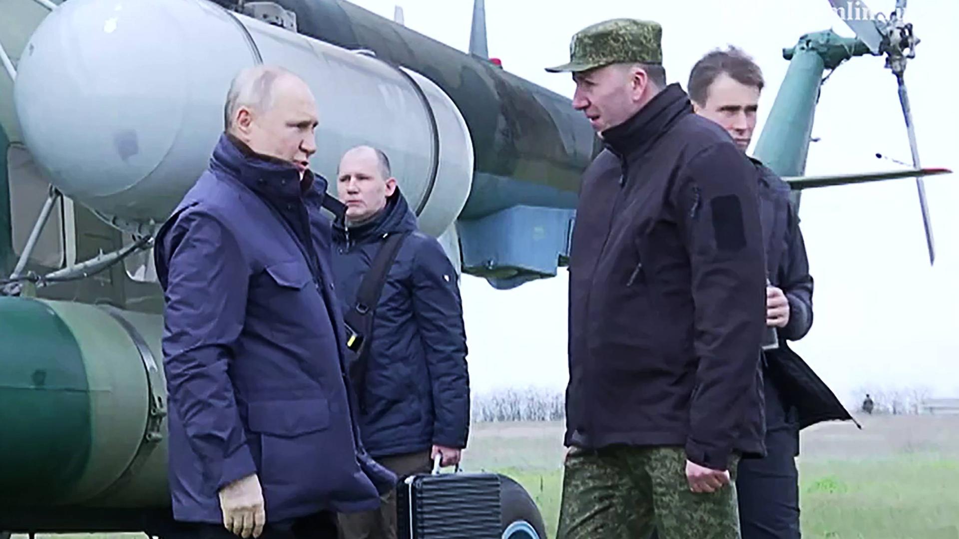 Der russische Präsident Putin steht mit einem Soldaten vor einem Militärhubschrauber und unterhält sich. Hinter ihnen stehen noch zwei Personen.