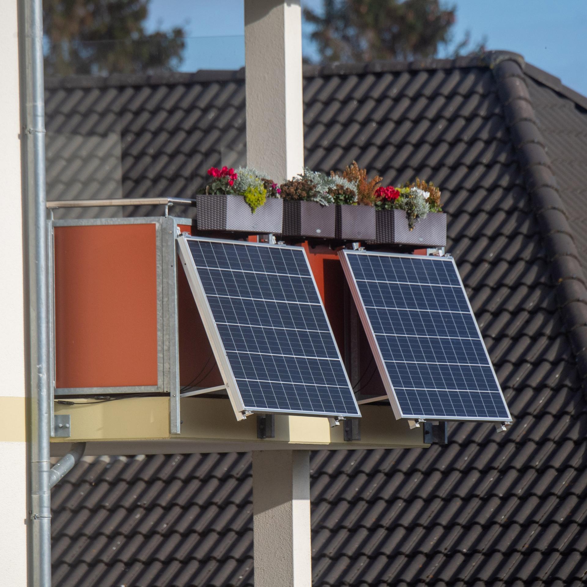 Solarmodule für ein sogenanntes Balkonkraftwerk hängen an einem Balkon unter bunt bepflanzten Blumenkästen.
