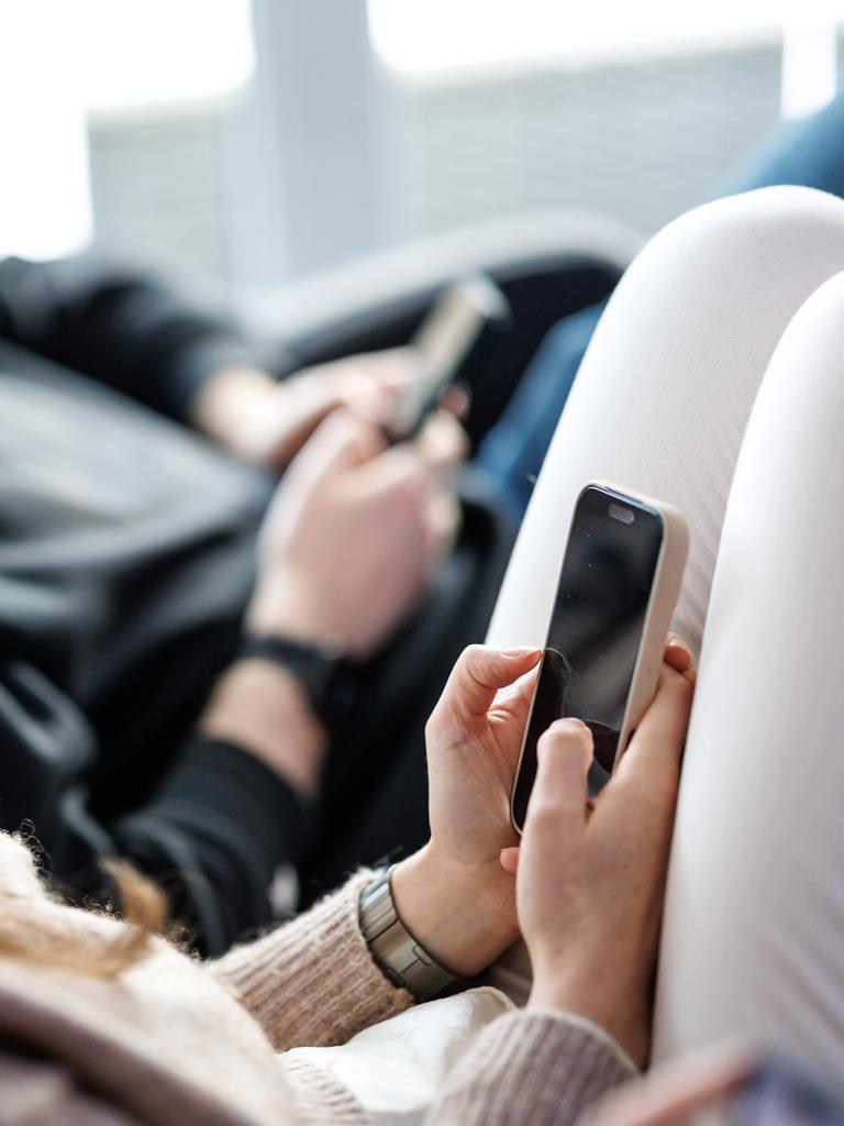 Eine junge Frau sitzt auf einem Sofa und benutzt ein Smartphone. Neben ihr sitzt ein junger Mann, der ebenfalls am Handy tippt. 
