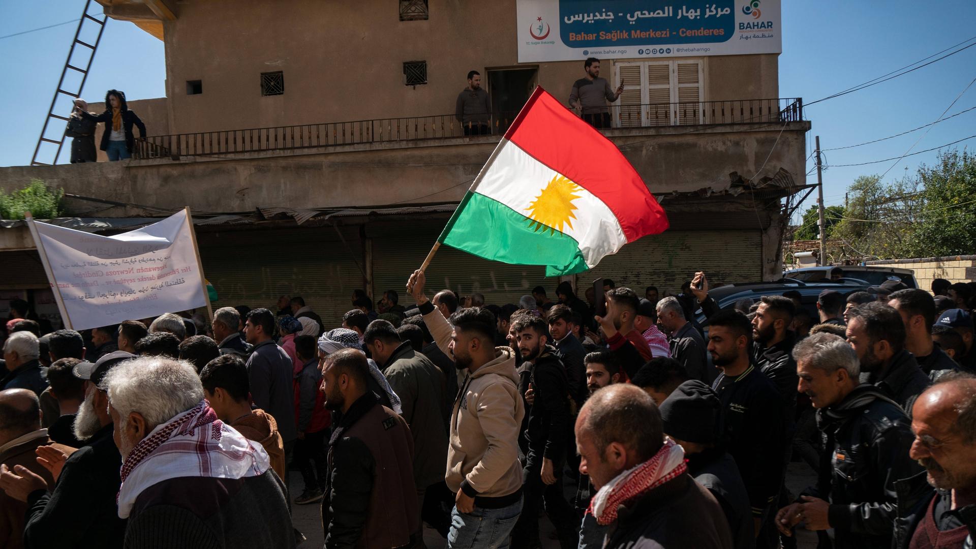 Ein Mann läuft als Mitglied in einem Beerdigungsumzug durch die Straßen und schwenkt eine kurdische Flagge.