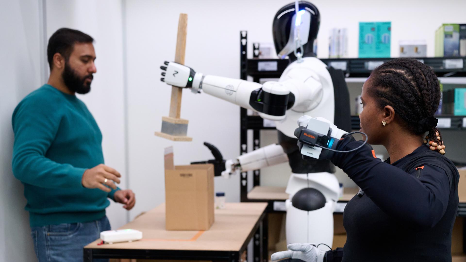 Mitarbeiter trainieren einen weißen Roboter, der mit einem Holzwerkzeug hantiert.