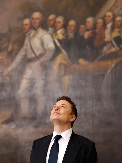 Elon Musk bei der Amtseinführung des US-Präsidenten Donald Trump in der Rotunde des US-Kapitols am 20. Januar 2025 in Washington, DC. Er blickt nach oben und steht vor einem riesigen historischen Gemälde.