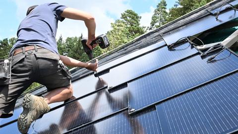 Ein Mann arbeitet an einem Photovoltaik-Modul auf einem Dach 
