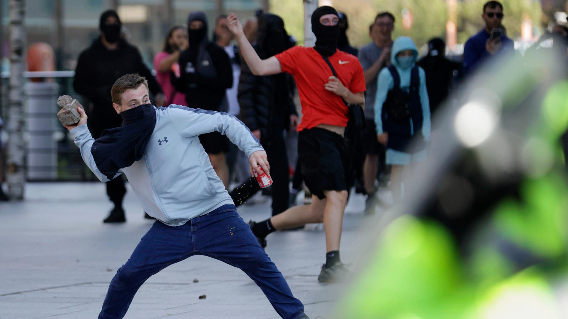 Vermummte Demonstranten in Liverpool, England. Einer ist dabei, einen Stein zu werfen.