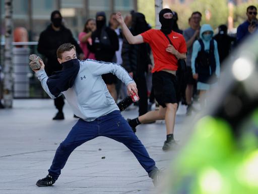 Vermummte Demonstranten in Liverpool, England. Einer ist dabei, einen Stein zu werfen.