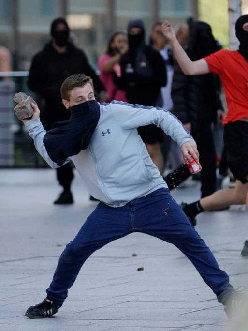 Vermummte Demonstranten in Liverpool, England. Einer ist dabei, einen Stein zu werfen.