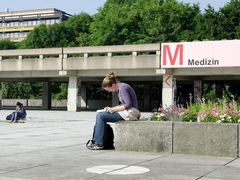Eine Medizin-Studentin in einer Vorlesungspause auf dem Campus: Sie ist über ihre Notizen gebeugt. Eine Medizin-Studentin in einer Vorlesungspause auf dem Campus: Sie ist über ihre Notizen gebeugt.