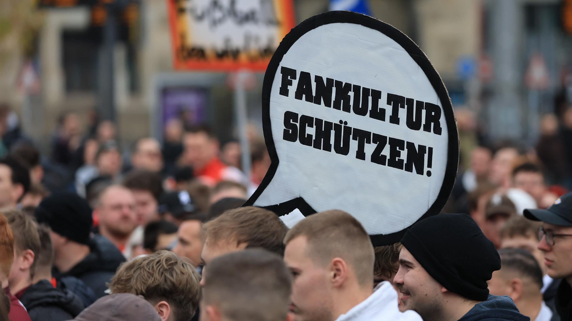 Blick auf eine größere Menge von Fans. Auf einem Schild in Form einer Sprechblase steht Fankultur schützen". Blick auf eine größere Menge von Fans. Auf einem Schild in Form einer Sprechblase steht Fankultur schützen".