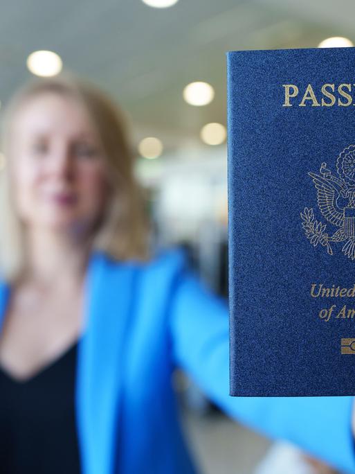 Eine Frau zeigt ihren US-amerikanischen Reisepass mit ausgestrecktem Arm.
