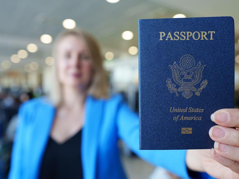 Eine Frau zeigt ihren US-amerikanischen Reisepass mit ausgestrecktem Arm.