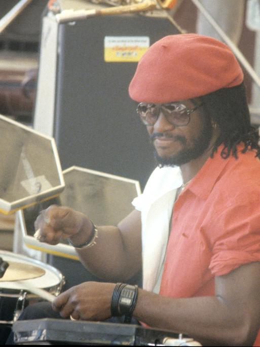 Der jamaikanische Schlagzeuger Sly Dunbar mit einem roten Hemd und einer roten Kappe an den Drums bei einem Konzert von "Sly & Robbie" in den 1980ern. 