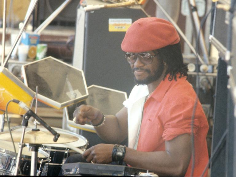 Der jamaikanische Schlagzeuger Sly Dunbar mit einem roten Hemd und einer roten Kappe an den Drums bei einem Konzert von "Sly & Robbie" in den 1980ern. 